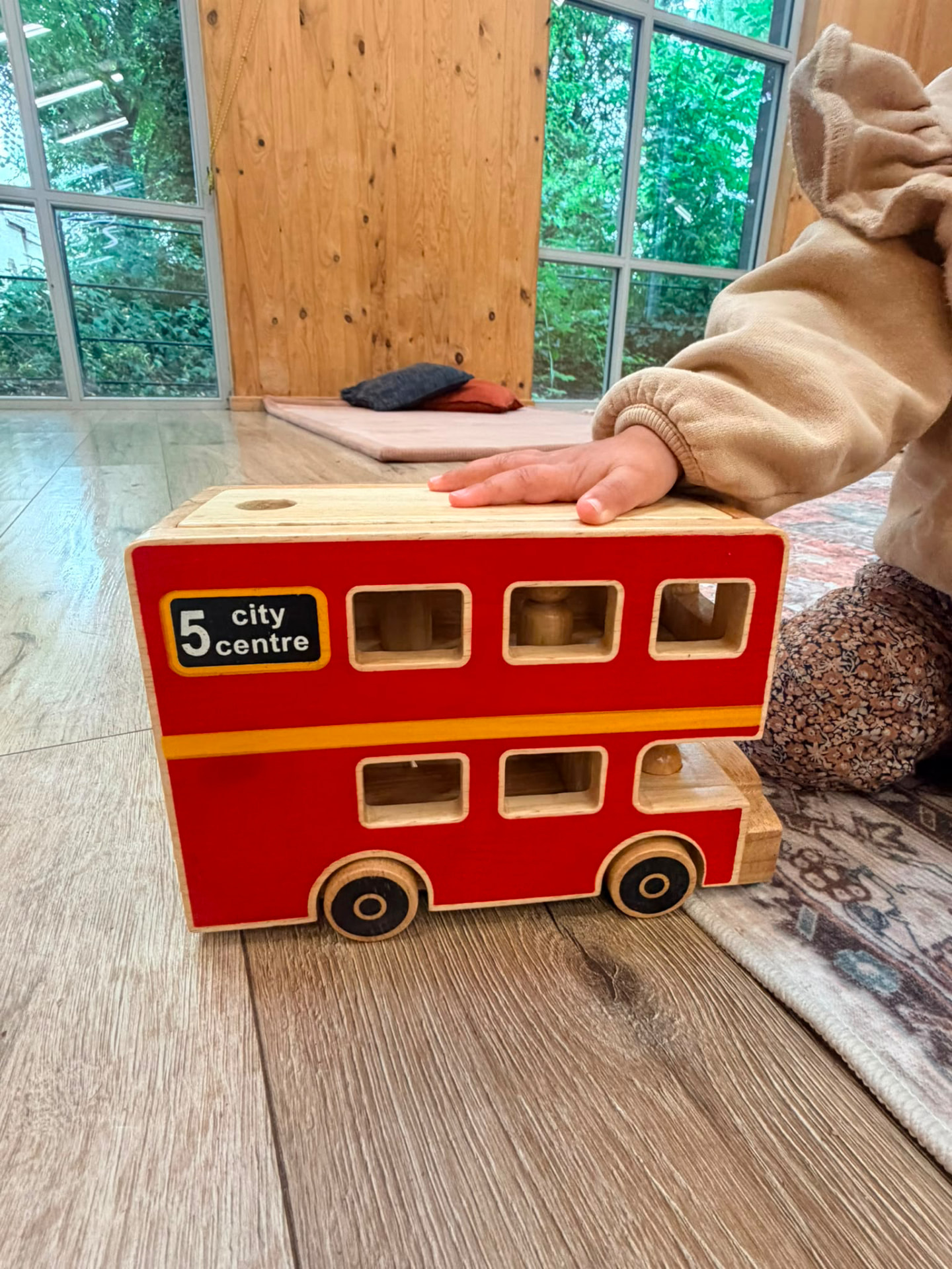 Little hand playing with a wooden red double-decker bus